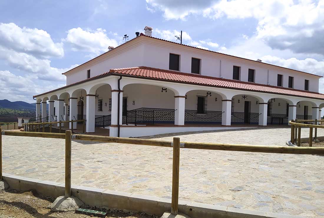 Un cortijo blanco con tejado de tejas rojas y un porche con arcos, en un día soleado.